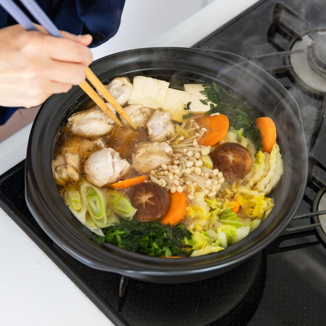 Nami from Just One Cookbook using chopsticks to cook a hot pot dish with various ingredients on a stove.