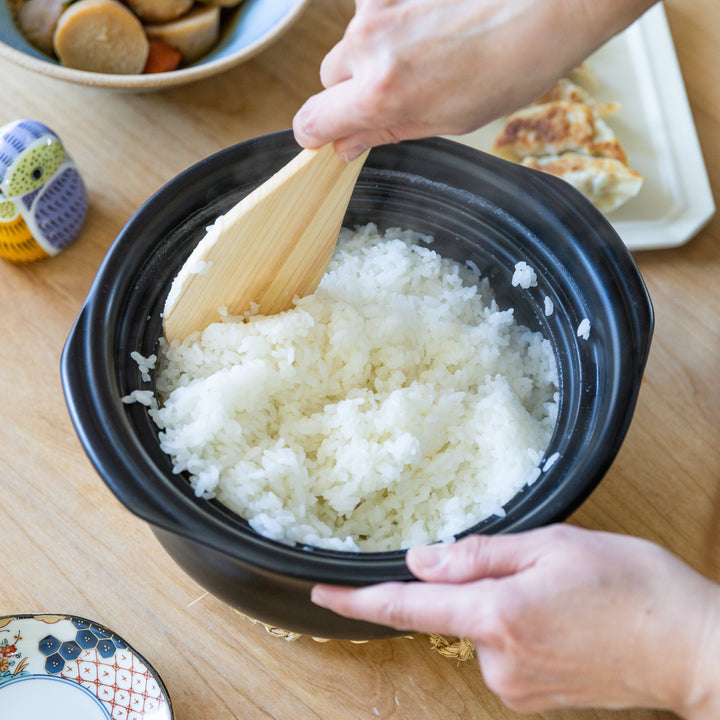 Freshly cooked Japanese rice inside navy donabe rice pot with wooden rice paddle