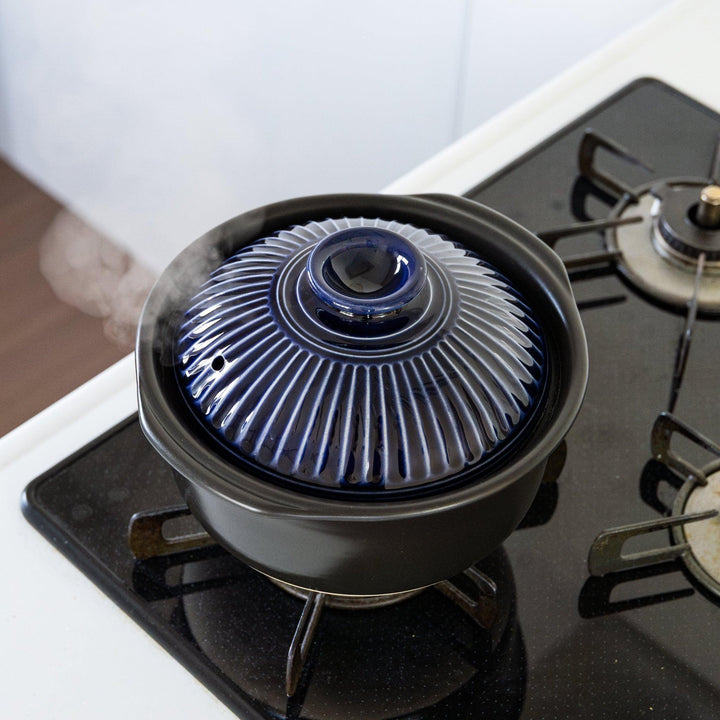 Navy Japanese donabe rice pot with blue lid cooking over gas stove flame