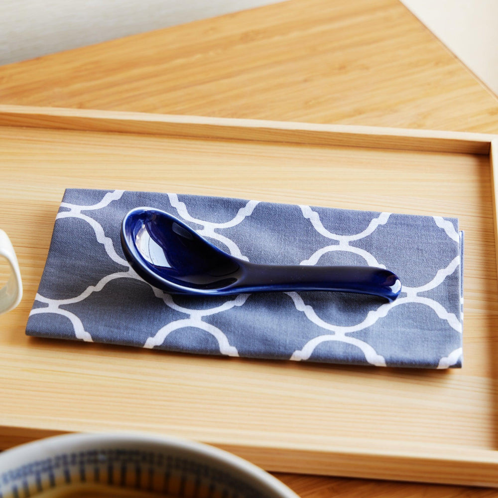 A blue ceramic spoon resting on a white and blue patterned tenugui, placed on a wooden tray.
