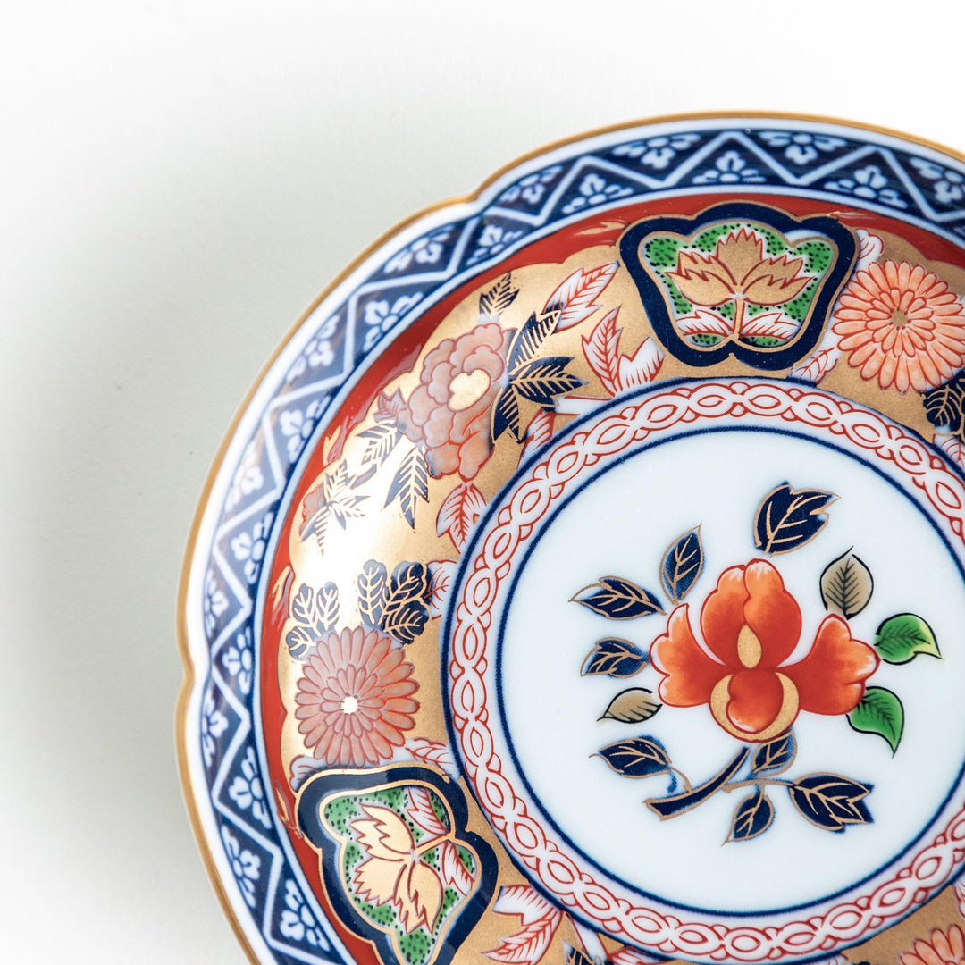 A round sauce dish with a central red floral motif, surrounded by a detailed border of gold, blue, and green floral patterns.