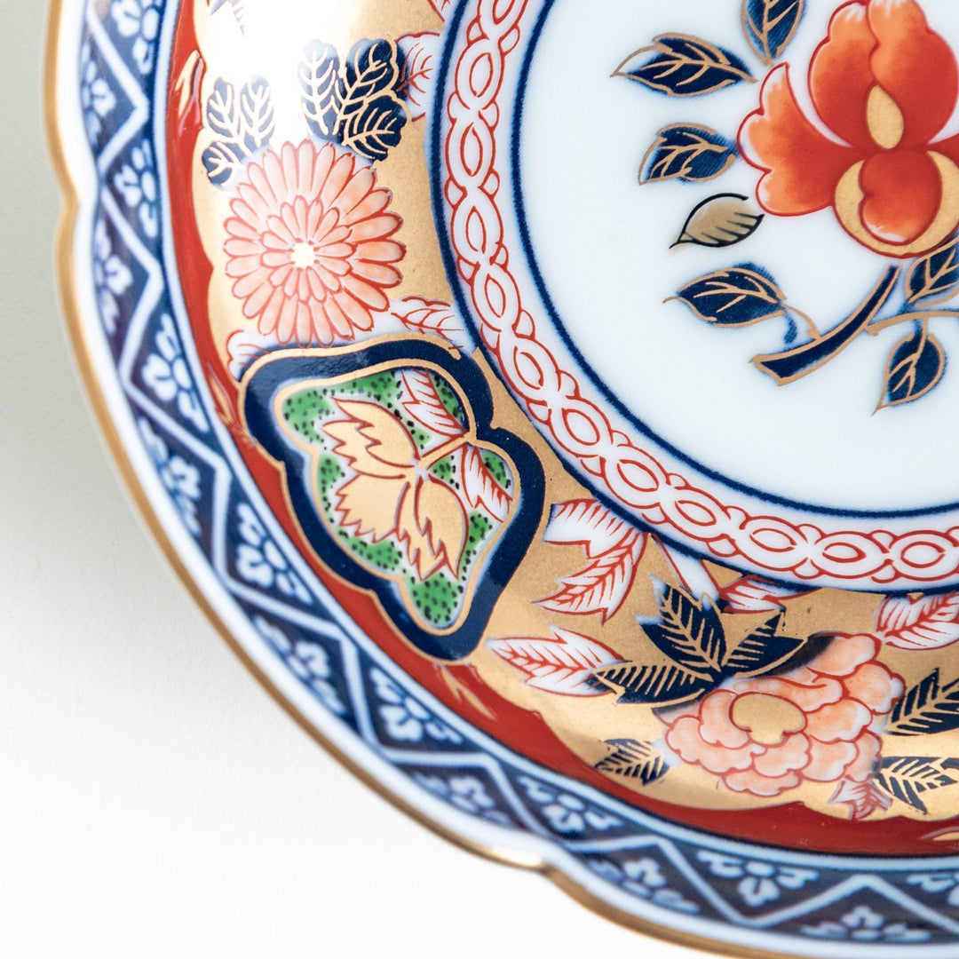 A round sauce dish with a central red floral motif, surrounded by a detailed border of gold, blue, and green floral patterns.