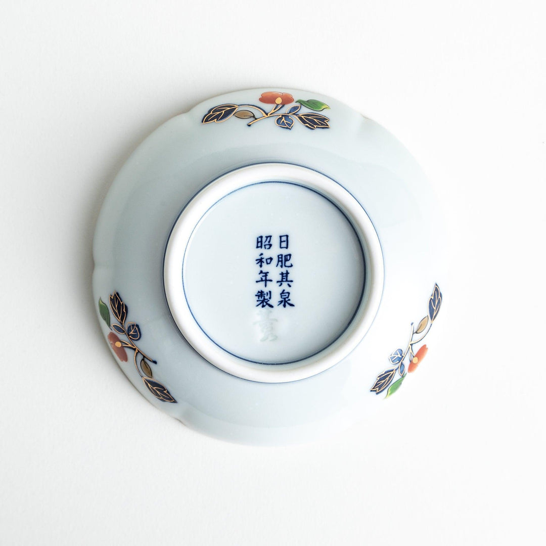 A round sauce dish with a central red floral motif, surrounded by a detailed border of gold, blue, and green floral patterns.