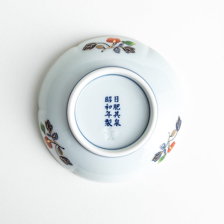 A round sauce dish with a central red floral motif, surrounded by a detailed border of gold, blue, and green floral patterns.