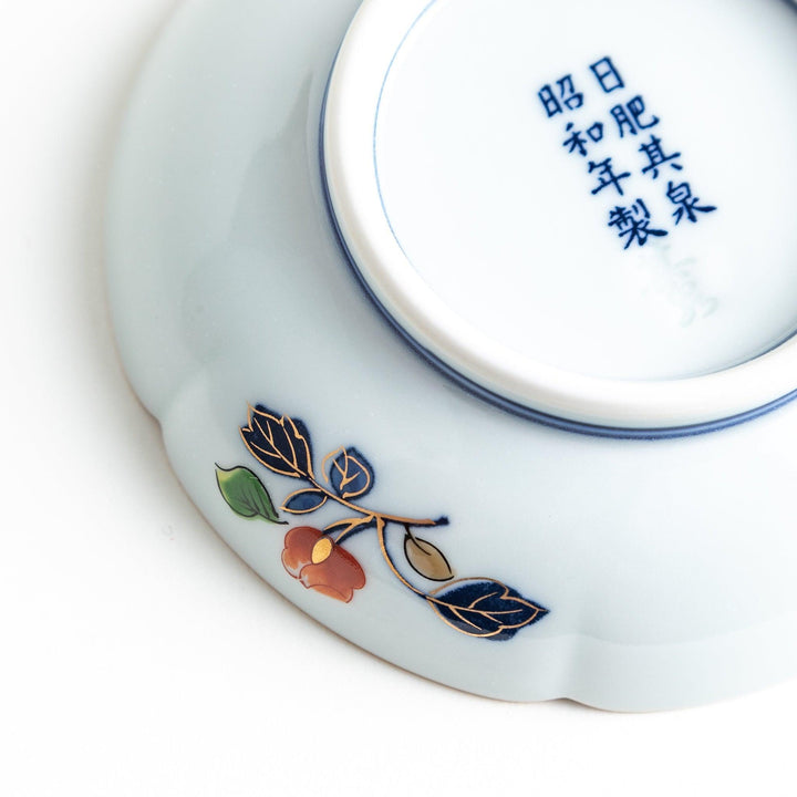 A round sauce dish with a central red floral motif, surrounded by a detailed border of gold, blue, and green floral patterns.