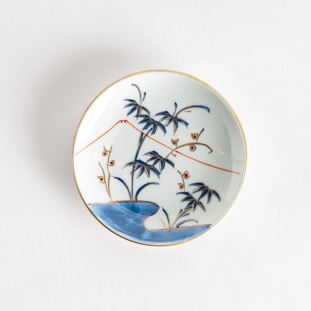 Round Japanese sauce dish with bamboo river and mountain scene in blue and orange tones with gold rim.
