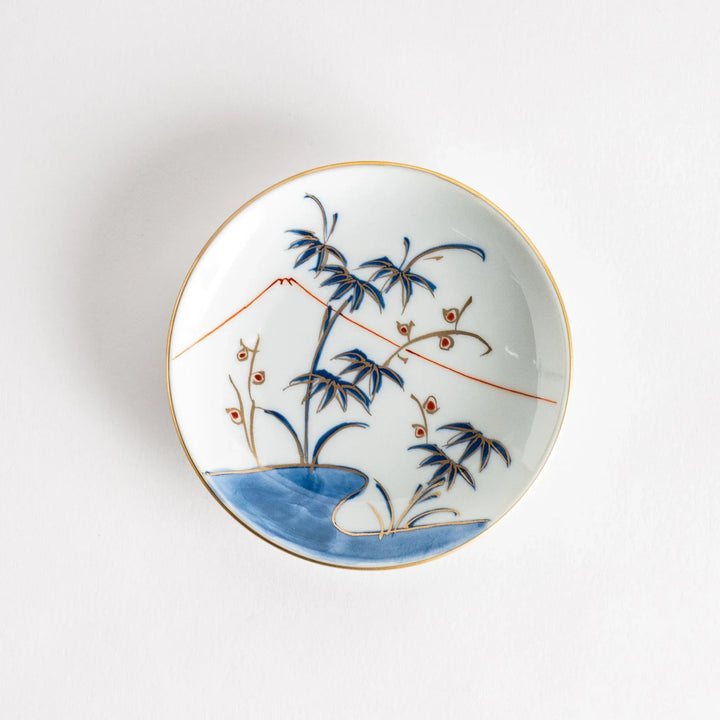 Round Japanese sauce dish with bamboo river and mountain scene in blue and orange tones with gold rim.