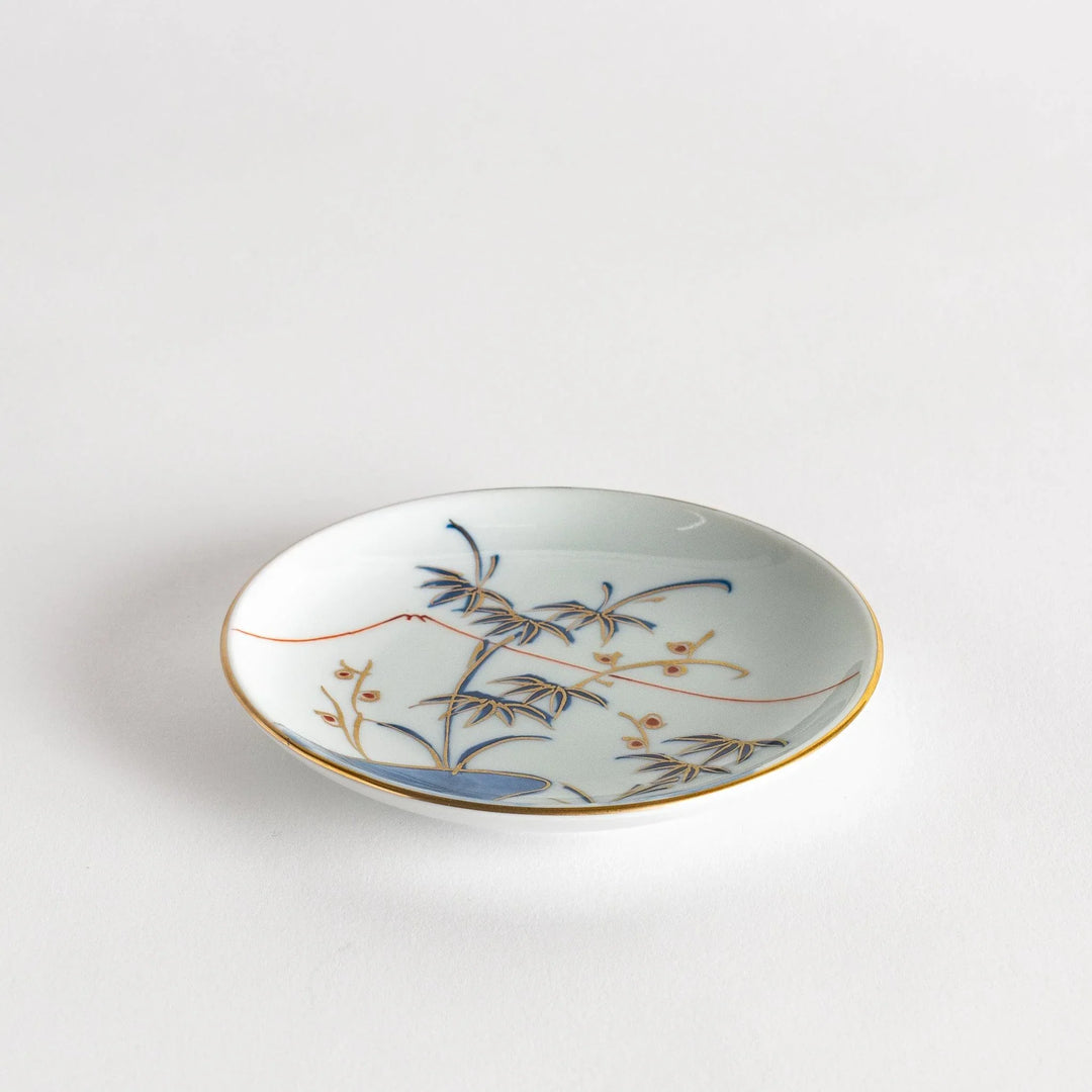 Round Japanese sauce dish with bamboo river and mountain scene in blue and orange tones with gold rim.
