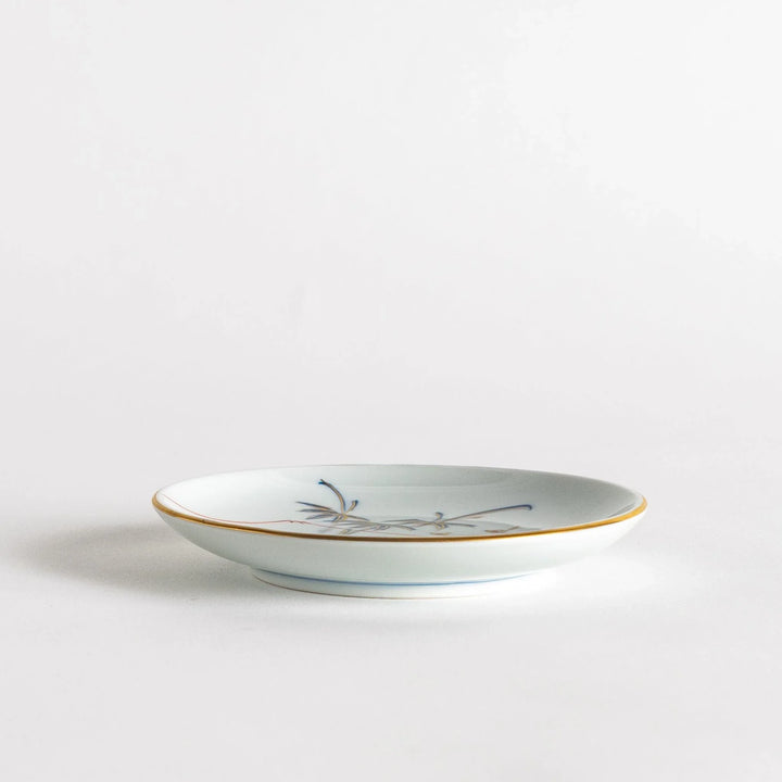 Round Japanese sauce dish with bamboo river and mountain scene in blue and orange tones with gold rim.