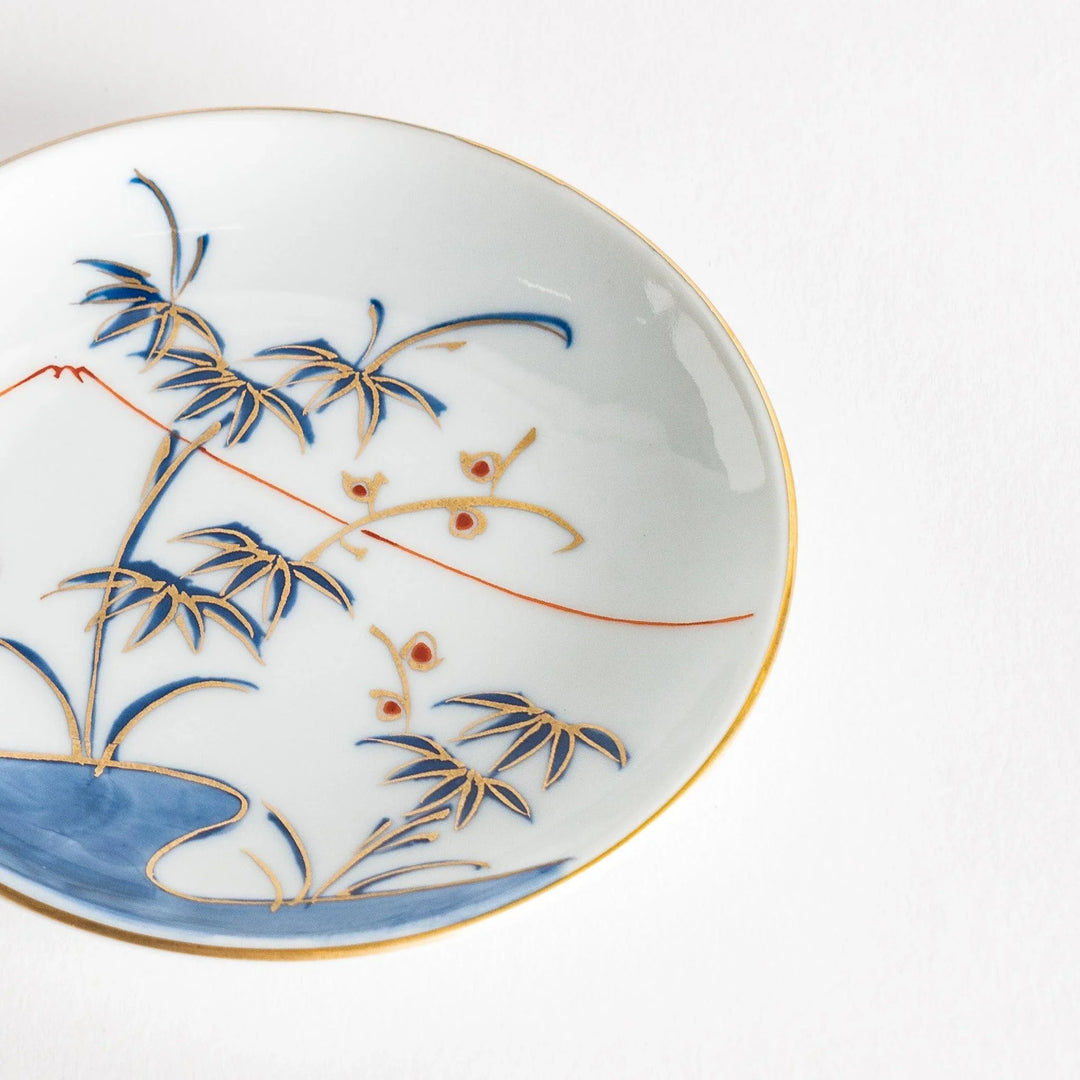 Round Japanese sauce dish with bamboo river and mountain scene in blue and orange tones with gold rim.