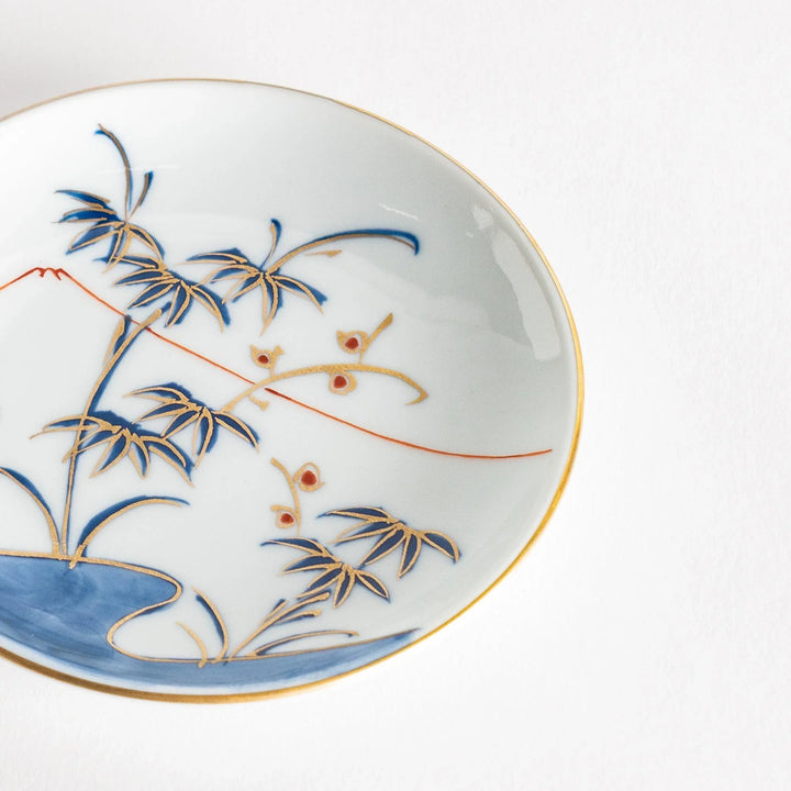 Round Japanese sauce dish with bamboo river and mountain scene in blue and orange tones with gold rim.