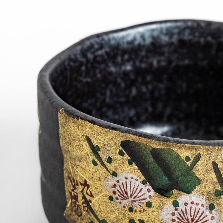 Matcha Bowl featuring a beautiful gold leaf and plum blossom design, set against a dark, textured background.