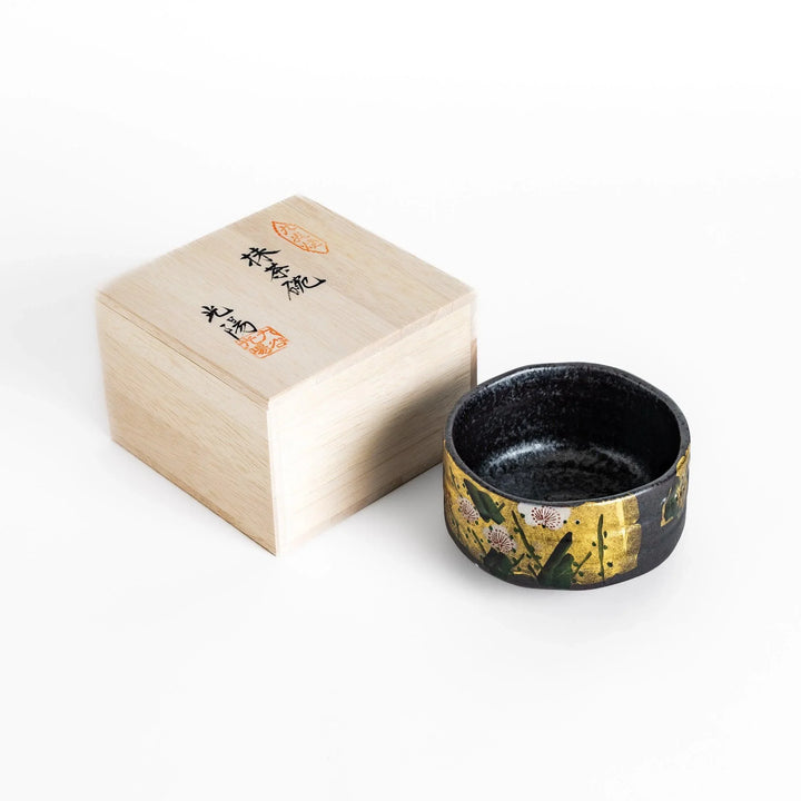 Matcha Bowl featuring a beautiful gold leaf and plum blossom design, set against a dark, textured background.