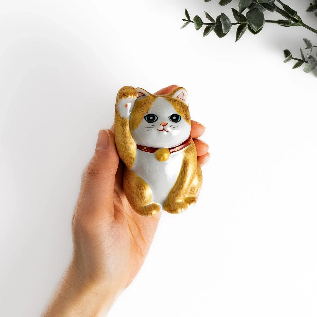 Maneki Neko figurine with a golden brush design, featuring a waving cat with a collar and bell for good luck.