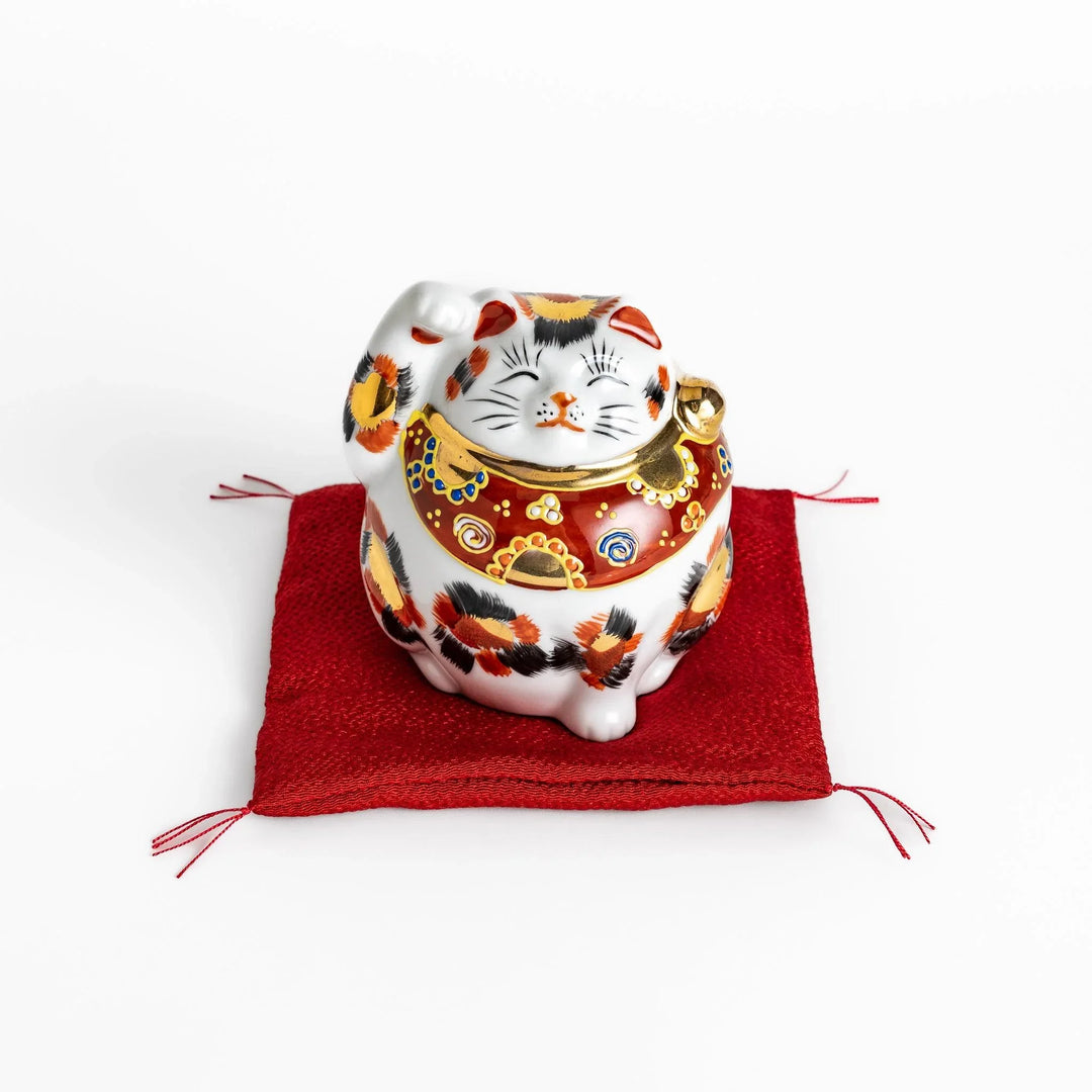 Maneki Neko figurine featuring a golden calico design, a raised paw, and a red patterned collar for good fortune.