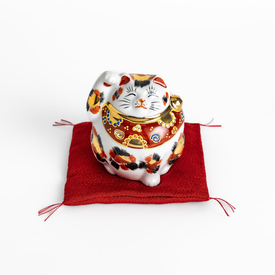 Maneki Neko figurine featuring a golden calico design, a raised paw, and a red patterned collar for good fortune.