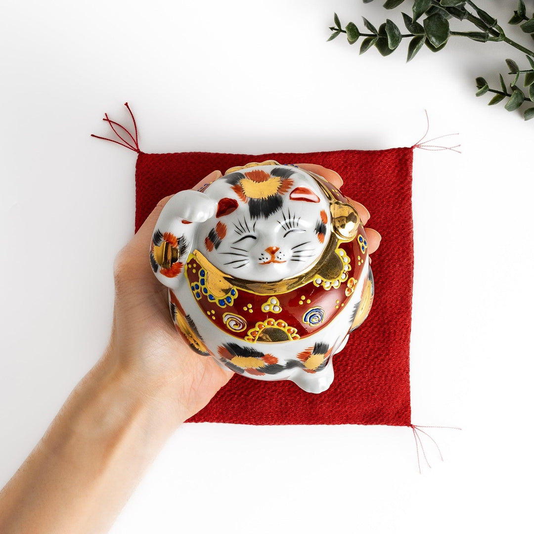Maneki Neko figurine featuring a golden calico design, a raised paw, and a red patterned collar for good fortune.