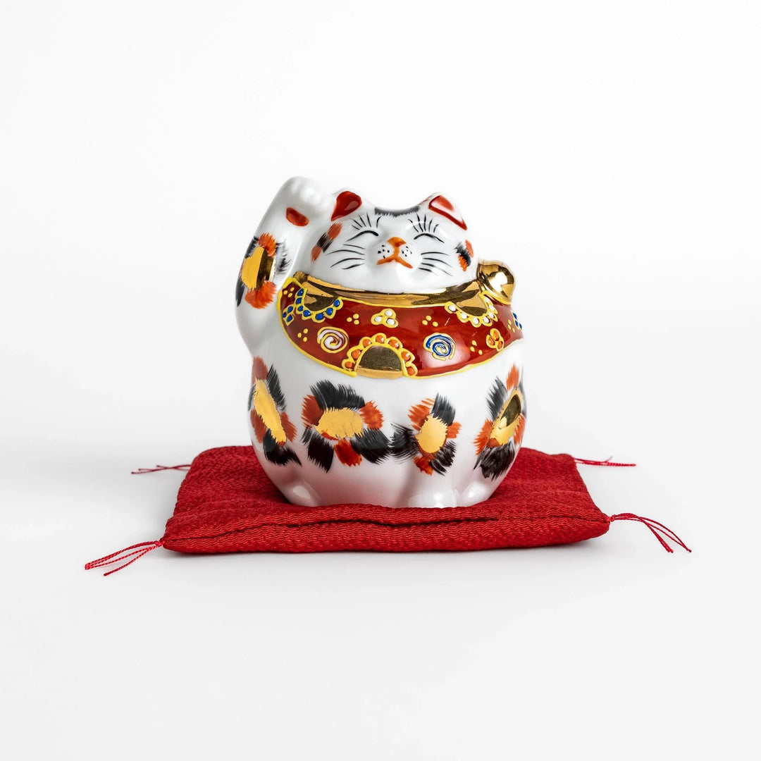 Maneki Neko figurine featuring a golden calico design, a raised paw, and a red patterned collar for good fortune.