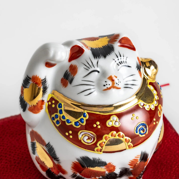 Maneki Neko figurine featuring a golden calico design, a raised paw, and a red patterned collar for good fortune.