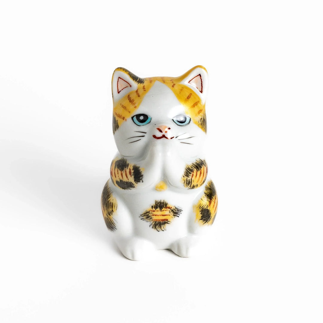 Maneki Neko figurine in a golden calico design, with a praying posture and blue eyes for good fortune.