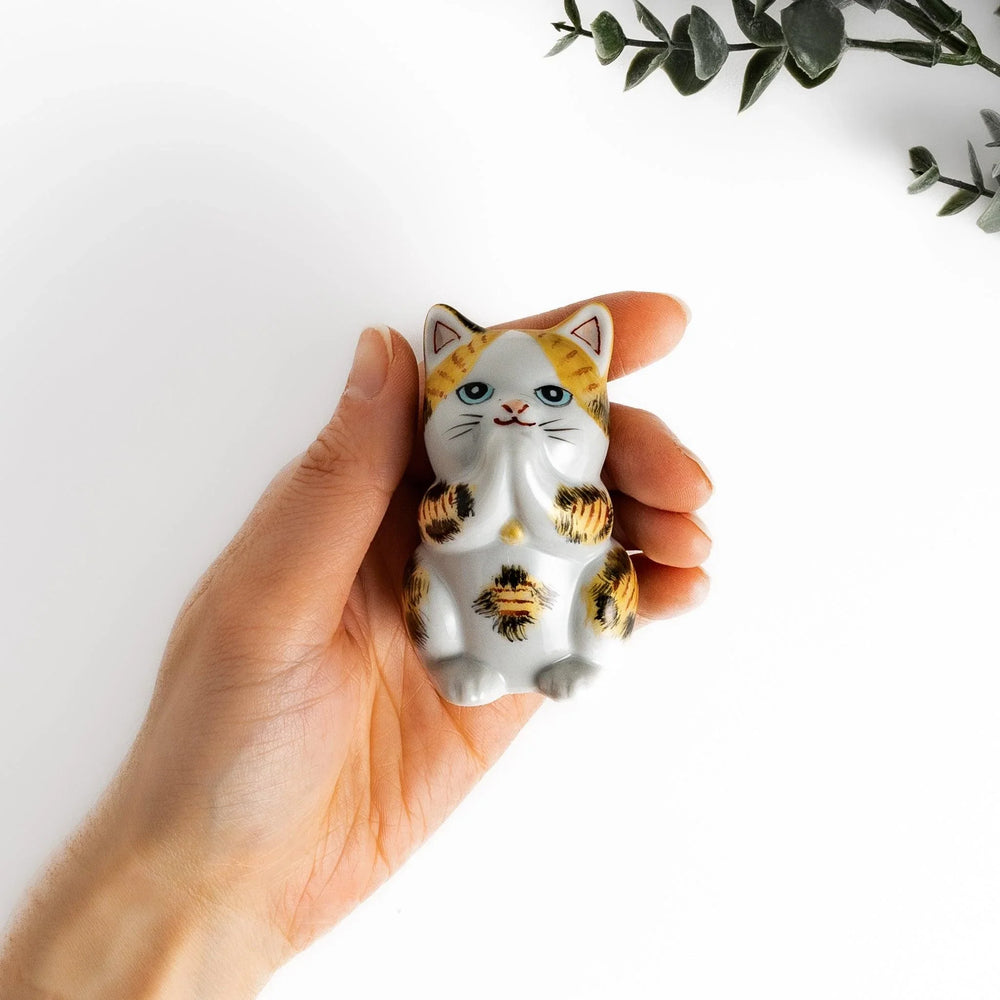 Maneki Neko figurine in a golden calico design, with a praying posture and blue eyes for good fortune.