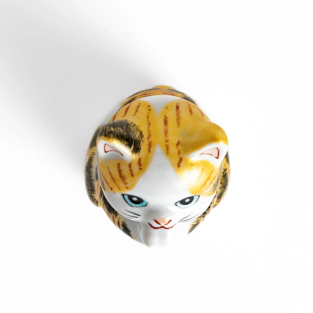 Maneki Neko figurine in a golden calico design, with a praying posture and blue eyes for good fortune.