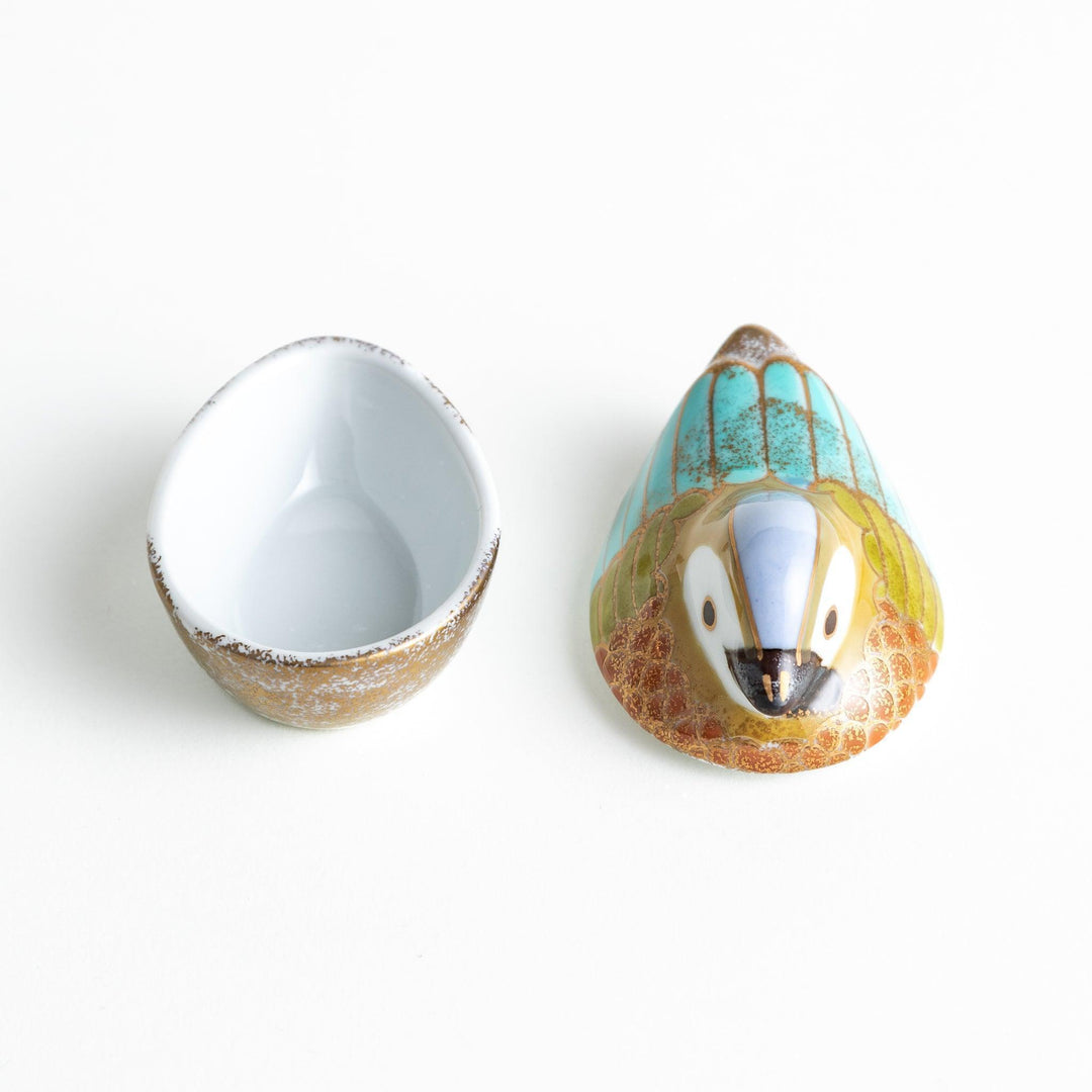 A small condiment bowl shaped like a hen, featuring a detailed painted design with blue, green, and gold accents.