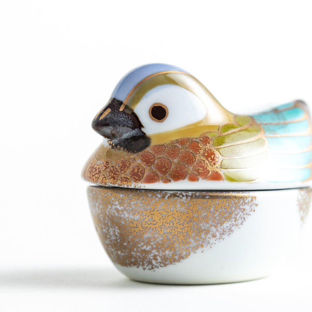 A small condiment bowl shaped like a hen, featuring a detailed painted design with blue, green, and gold accents.