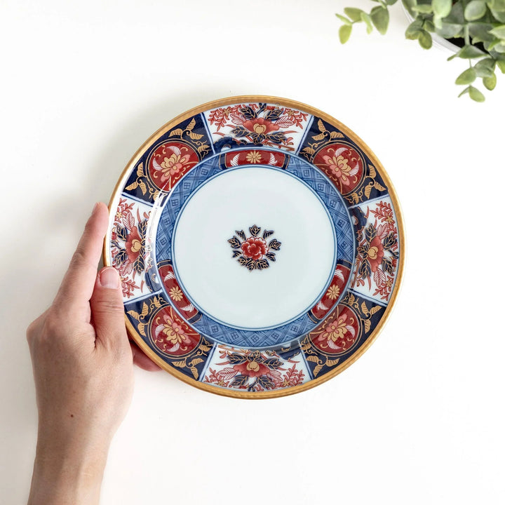 Japanese Imari style porcelain plate with central floral motif and ornate red blue and gold rim pattern.