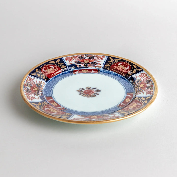 Japanese Imari style porcelain plate with central floral motif and ornate red blue and gold rim pattern.