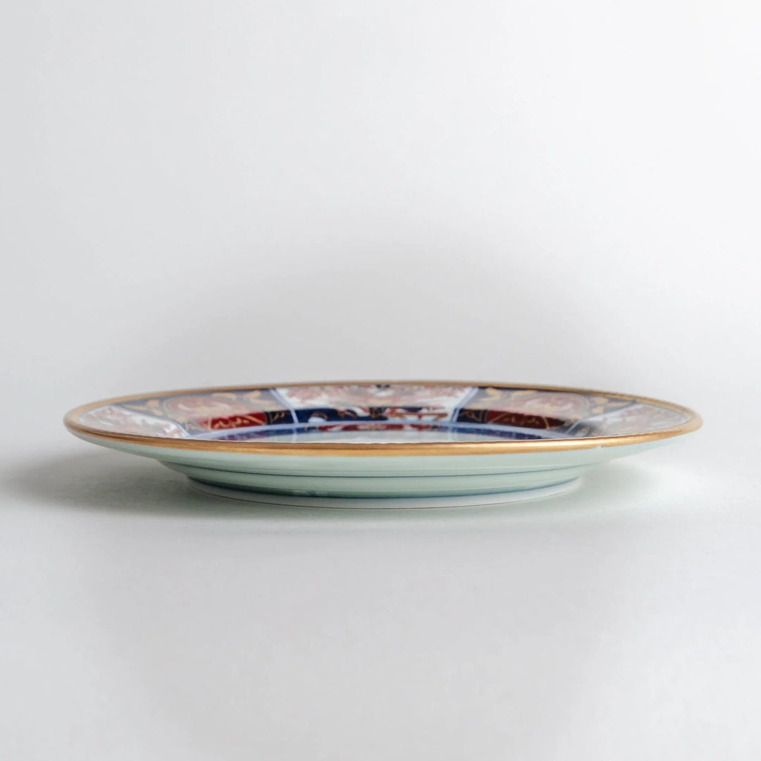 Japanese Imari style porcelain plate with central floral motif and ornate red blue and gold rim pattern.