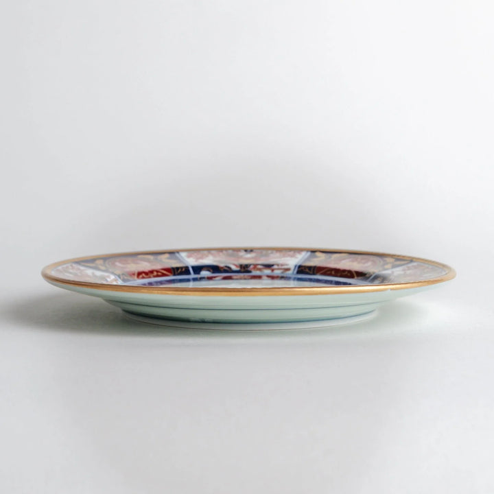 Japanese Imari style porcelain plate with central floral motif and ornate red blue and gold rim pattern.