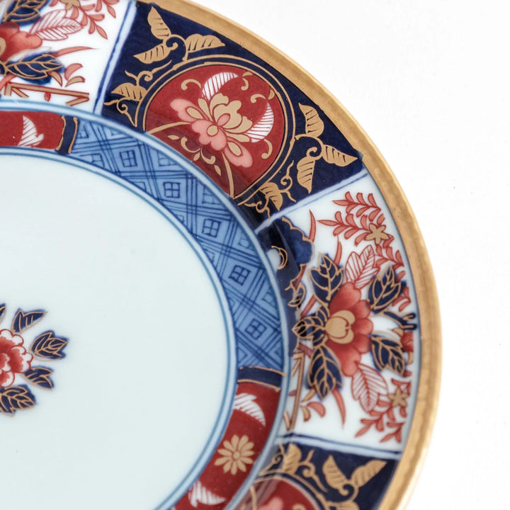 Japanese Imari style porcelain plate with central floral motif and ornate red blue and gold rim pattern.