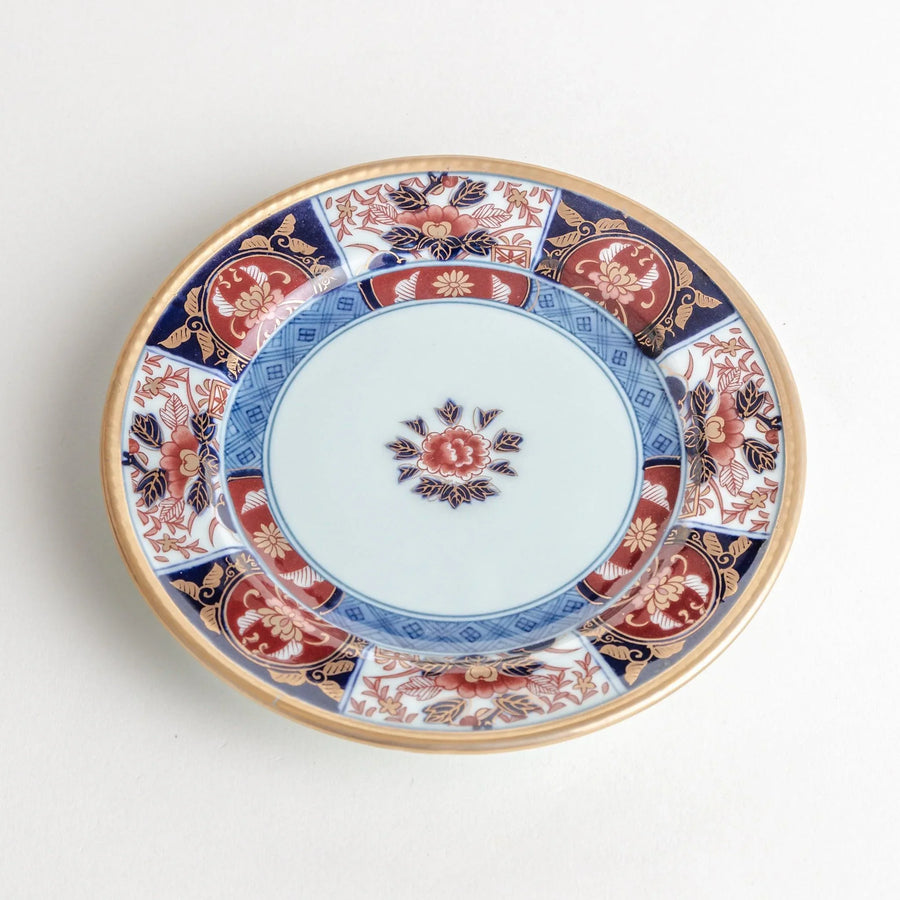 Small Japanese porcelain plate with Imari style floral design and alternating red blue and gold patterns.