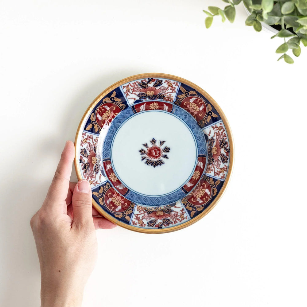 Small Japanese porcelain plate with Imari style floral design and alternating red blue and gold patterns.