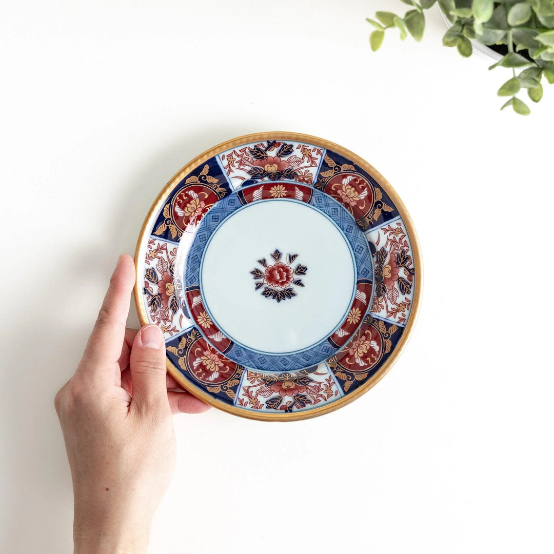 Small Japanese porcelain plate with Imari style floral design and alternating red blue and gold patterns.
