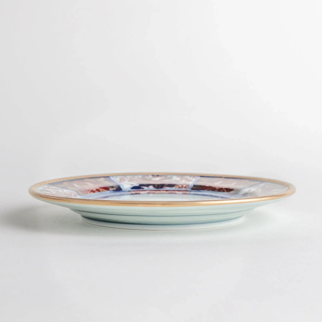 Small Japanese porcelain plate with Imari style floral design and alternating red blue and gold patterns.