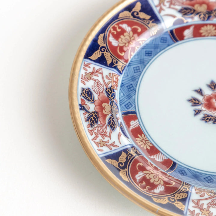 Small Japanese porcelain plate with Imari style floral design and alternating red blue and gold patterns.