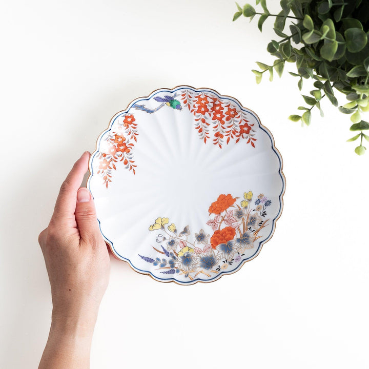 Round scalloped salad plate with floral designs in red yellow and blue and wisteria branch at the top.