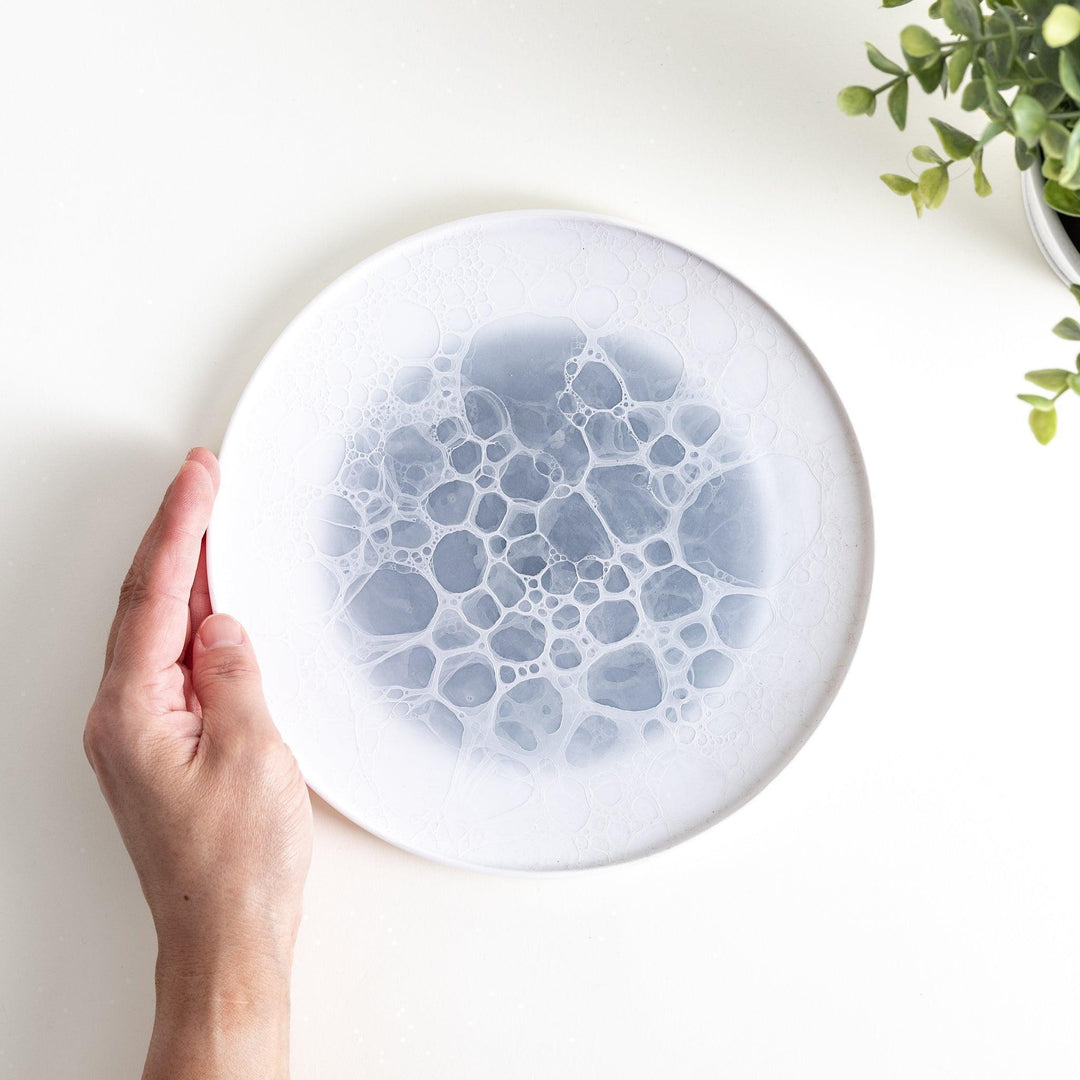 A white salad plate featuring a unique bubble design in shades of blue, resembling frothy ocean waves.