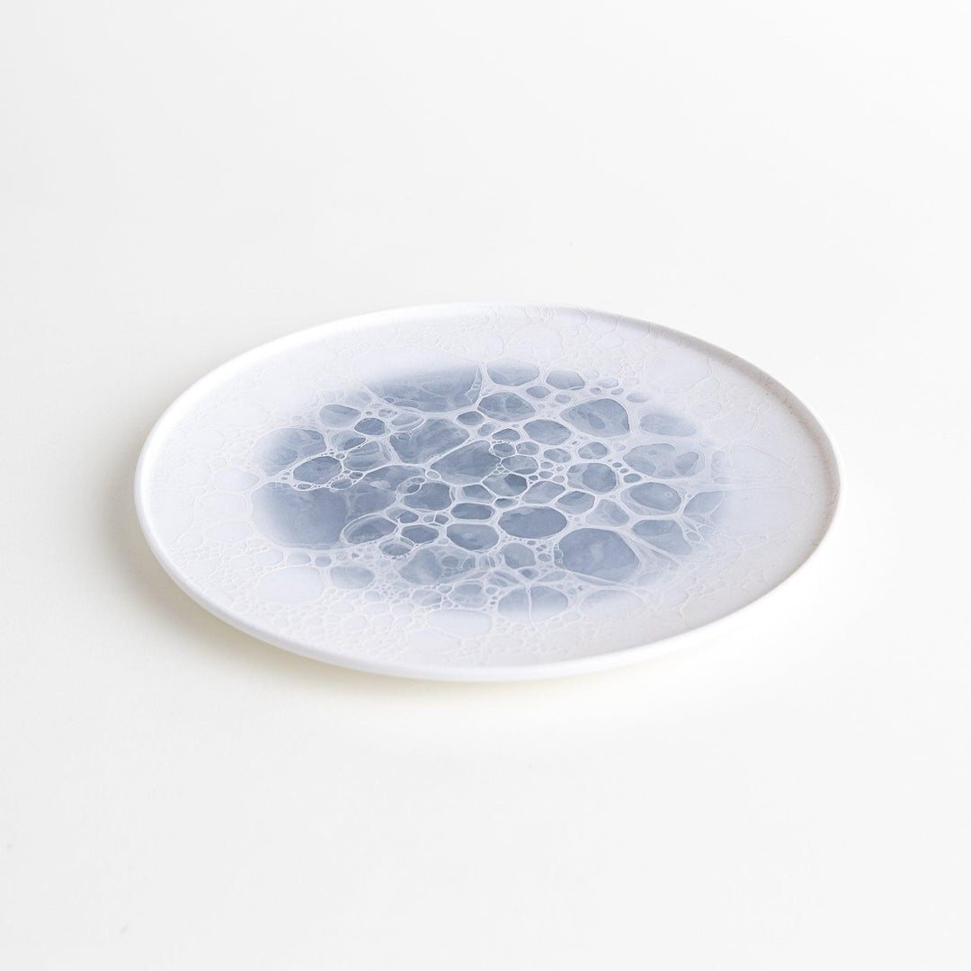 A white salad plate featuring a unique bubble design in shades of blue, resembling frothy ocean waves.