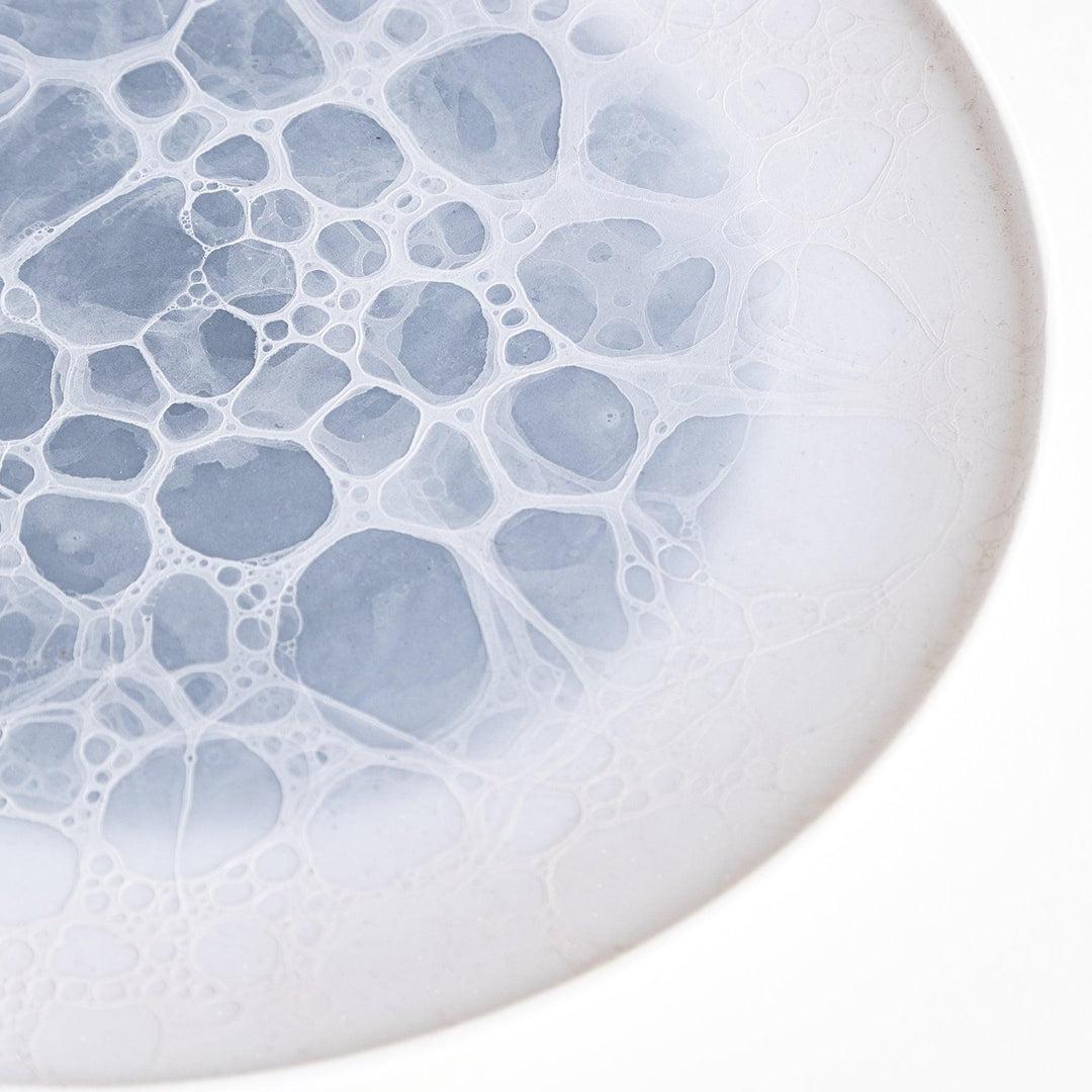 A white salad plate featuring a unique bubble design in shades of blue, resembling frothy ocean waves.