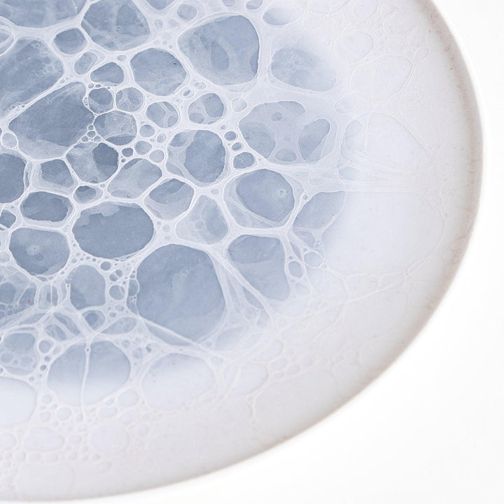 A white salad plate featuring a unique bubble design in shades of blue, resembling frothy ocean waves.