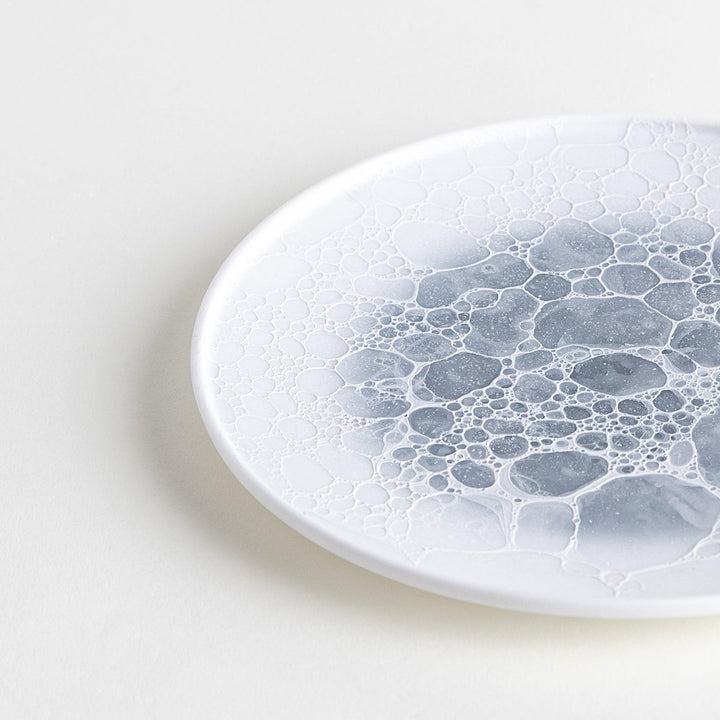 A white dessert plate featuring a unique bubble design in shades of blue, resembling frothy ocean waves.