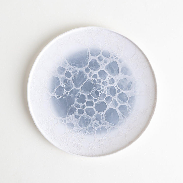 A white salad plate featuring a unique bubble design in shades of blue, resembling frothy ocean waves.