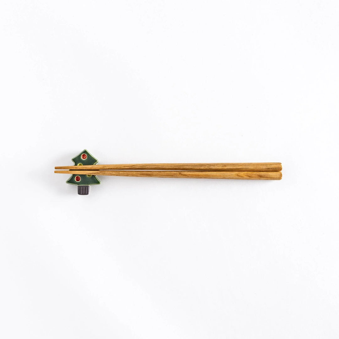 The green Christmas tree chopsticks rest with chopsticks resting on it, photographed from a distance.