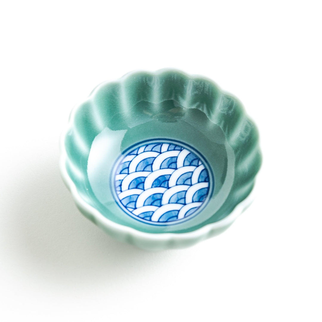 A small green cereal bowl with a scalloped edge and a blue and white wave pattern in the center.