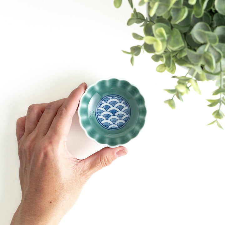 A small green cereal bowl with a scalloped edge and a blue and white wave pattern in the center.