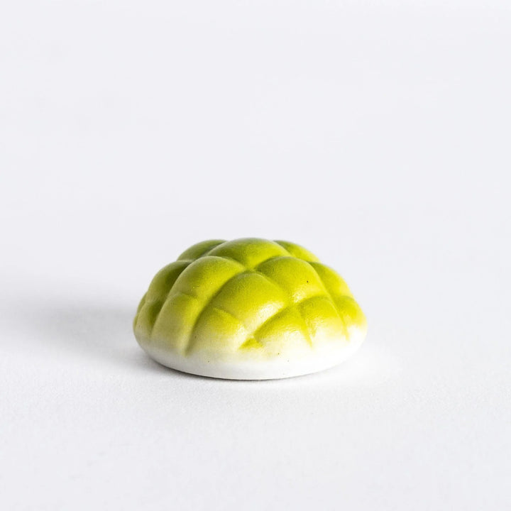 Green melon pan shaped ceramic chopstick rest with textured top and golden accents adding sweet playful touch.