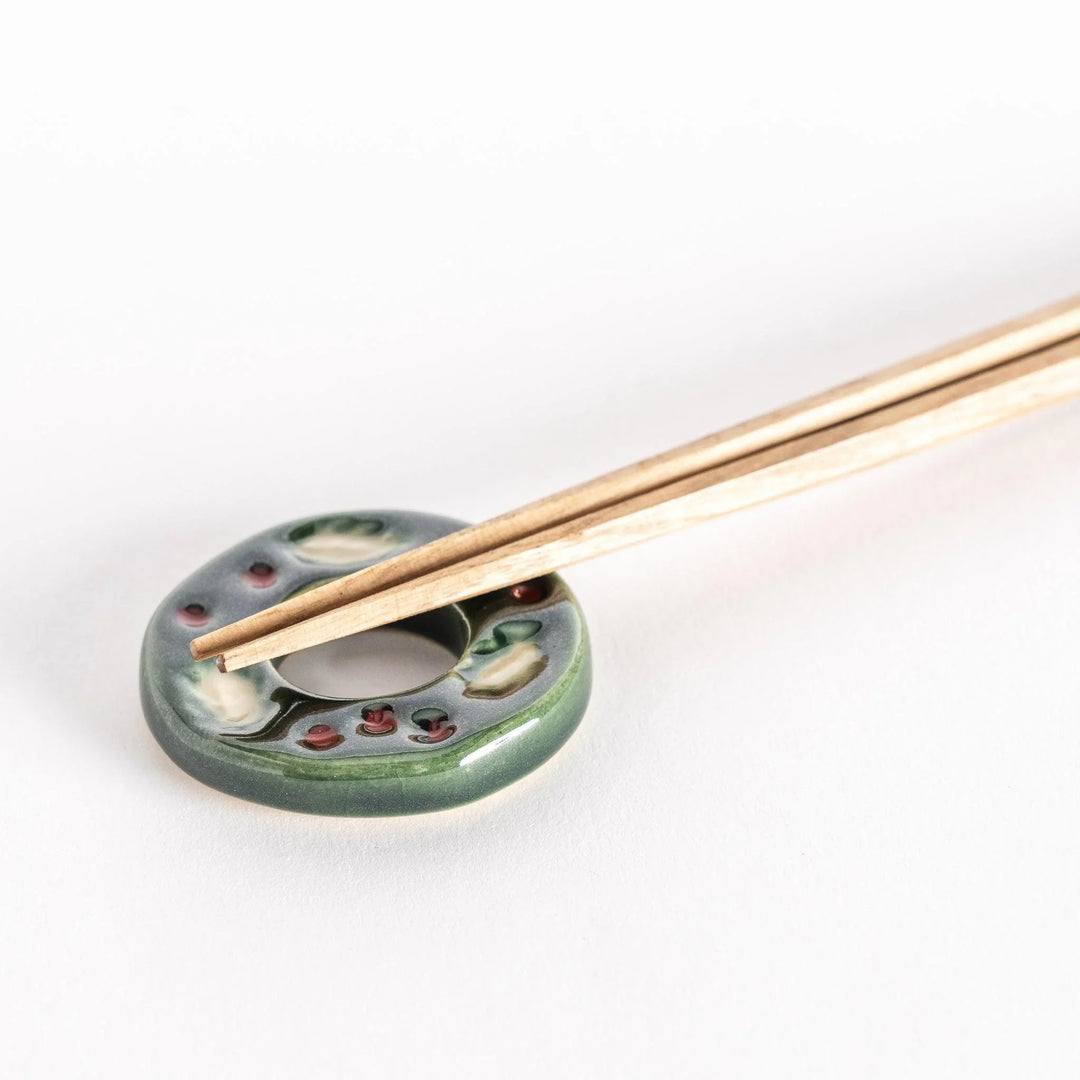 Green wreath shaped ceramic chopstick rest with detailed leaves adding festive touch to table.
